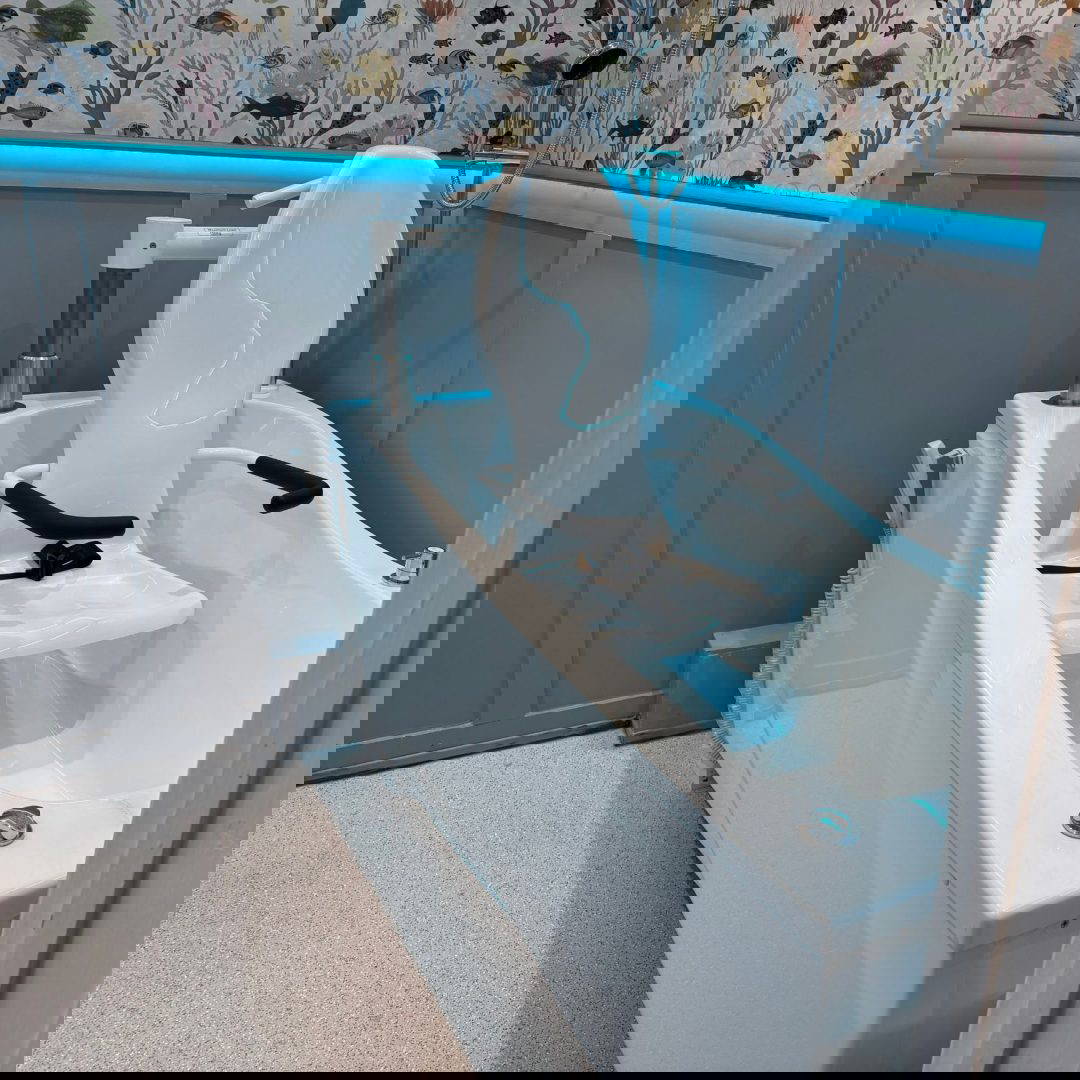 Image of bath in a bathroom with blue wooden panelling and colourful lights.