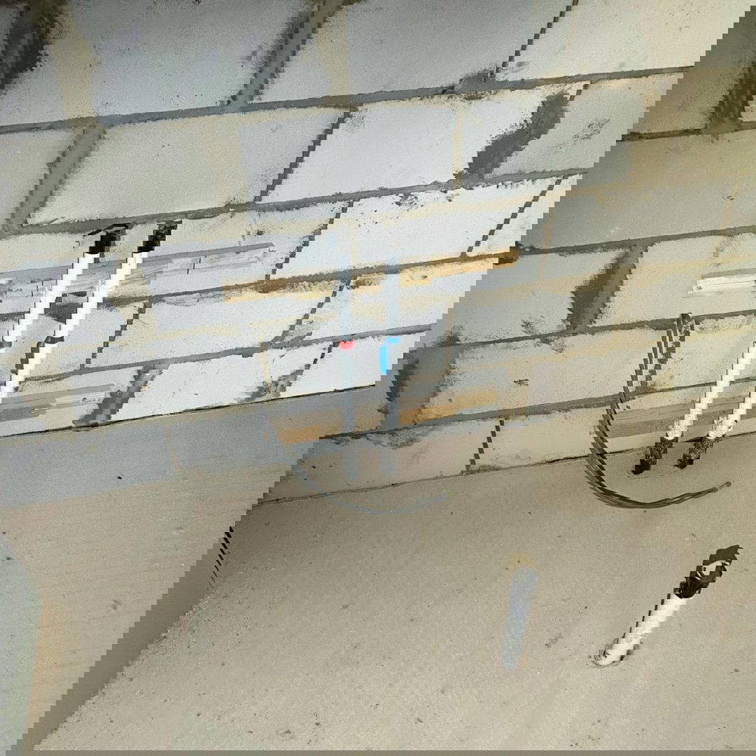 An image of a bathroom being constructed, with a concrete floor and concrete block walls. In the floor there are two pipes, one for the hot water and one for cold.